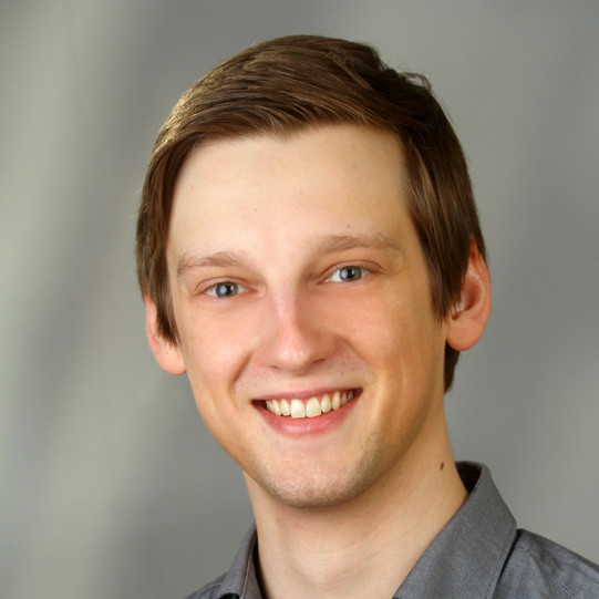 Portrait eines lächelnden Mirko Spiegels vor grauem Hintergrund