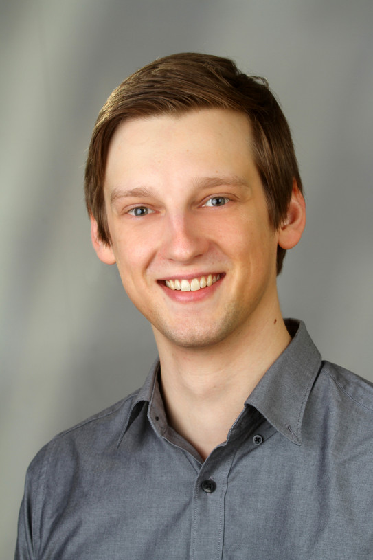 Portrait eines lächelnden Mirko Spiegels vor grauem Hintergrund