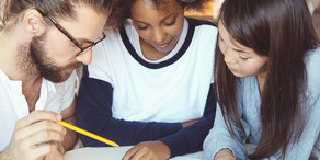 Drei Studierende haben ihre Köpfe über Unterlagen zusammengesteckt.
