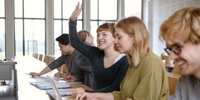 Five students sitting in the seminar room at the table. A female student raises her hand.